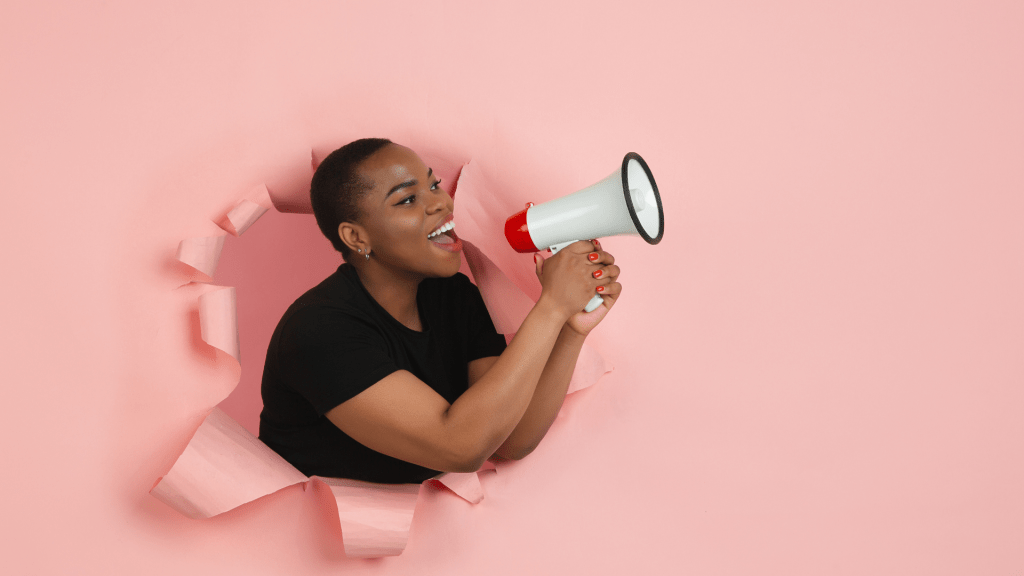 Woman talking into loudspeaker while bursting out of pink wall